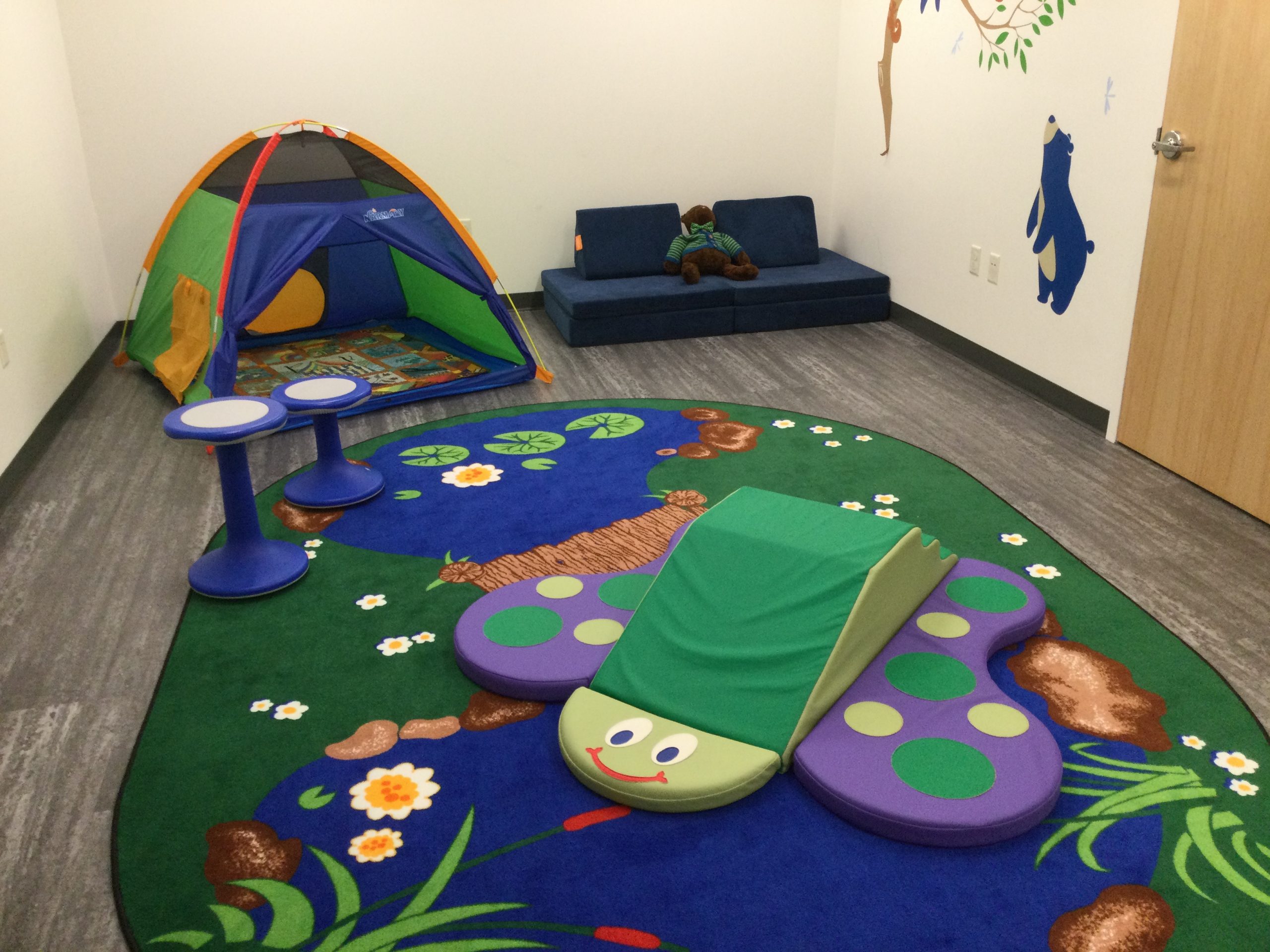 Inside the Sensory Space featuring a tent, couch, wobble stools, butterfly climber, and outdoors rug.