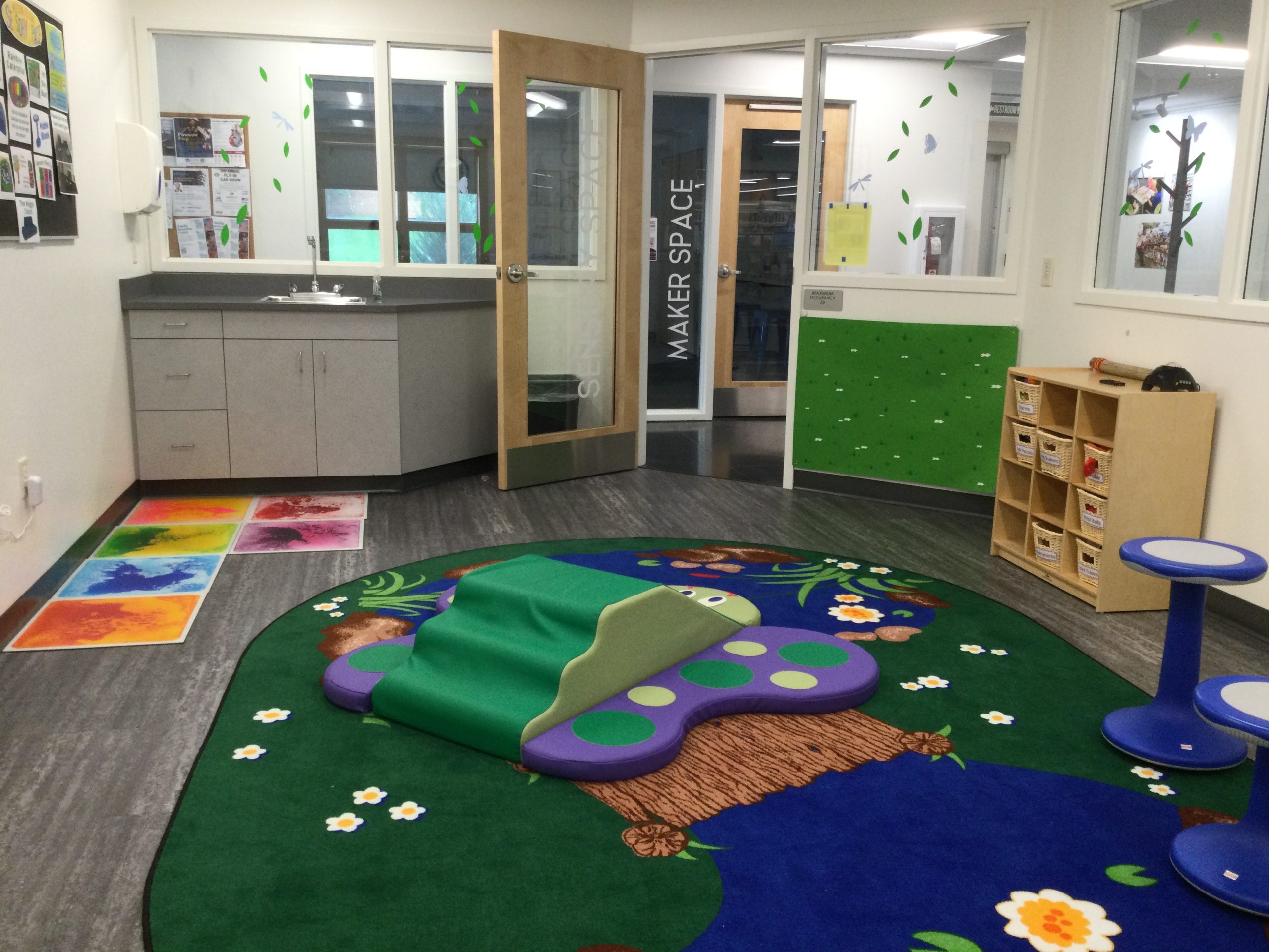 Inside the Sensory Space, featuring colorful tiles, butterfly climber, felt board, outdoors rug, sink and door.