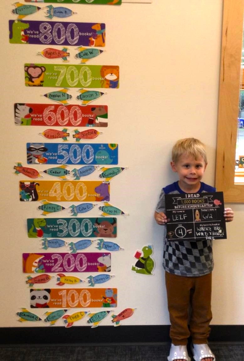 A child next to our 1000 books before kindergarten wall after completing the challenge.